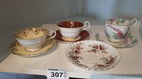 Three teacups and four saucers displayed, showing different floral patterns with gold trim on bone china.