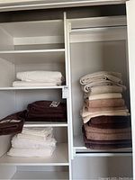 Two shelving units showing neatly folded stacks of white, cream, brown, and beige towels and linens