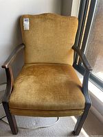 Front view of mustard yellow upholstered armchair with wooden legs and arms.