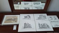 Five prints on a wooden table under a mirror, showing multiple cityscape and architectural sketches in black and white and sepia tone.