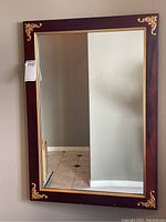 Full view of rectangular wall mirror with wood frame and decorative gold corner accents.