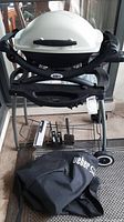 Grill assembled on wheeled stand with cover and accessories below