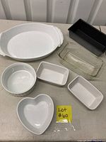 Top-down photo showing all pans together: large ceramic dish with handles, black metal loaf pan, clear glass loaf pan, round soufflé dish, heart-shaped dish, and two small mini loaf pans.