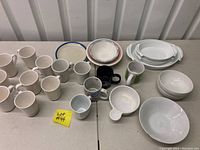 Photo showing coffee mugs including nine white Oneida mugs, Bistro Blanc mug, decorative mugs, and white bowls and dishes