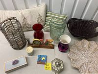 Lot of decorating items: pillows, glass vases in various colors, wicker and star-shaped baskets, wooden LOVE sign, glass box, southwestern decorative box, and candle holder.