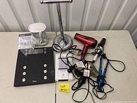 Photo showing full lot items arranged on table including scale, toilet paper holder, water flosser, hair tools and accessories