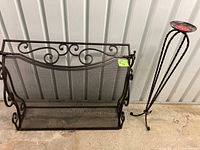 Fireplace grate and tall candlestick displayed side by side on concrete floor with metal siding background