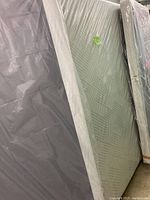 King mattress and split platform base wrapped in plastic, showing mattress surface pattern and platform base color.