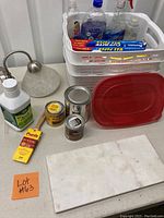 Overall view of kitchen and home items showing granite cutting board, three storage containers, wall sconce, cleaning and paint supplies.