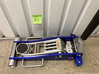 Full side view of the blue aluminum floor jack in collapsed position showing wheels and frame
