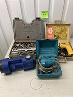 Full view of the lot showing Craftsman ratchet set, DeWalt drill, Makita sander, and Campbell Hausfeld compressor on a surface with a green lot tag.