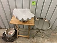 Small collapsible wooden side table, metal collapsible side table with round tray, and large decorative shell on wooden table