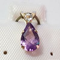 Front close-up photo of pear-shaped purple amethyst pendant set in 10K yellow gold with clear round gemstone above.