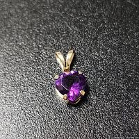 Close-up photo of a heart-shaped amethyst pendant in 10K yellow gold on black background.