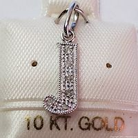 Close-up front view of 10K white gold diamond 'J' pendant on jewelry display card