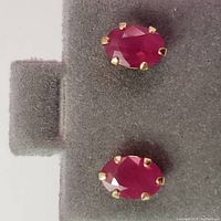 Top view of the pair of oval ruby earrings set in 10K yellow gold with six prongs on gray jewelry display pad.