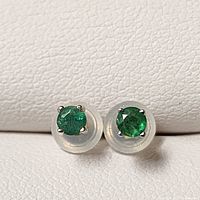 Front view of both emerald stud earrings showing round green stones and four-prong white gold settings.