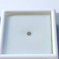 Top view of a single loose round diamond on white cushioned base inside a transparent white frame case.
