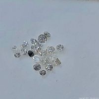 Photo of multiple small loose diamonds on a white surface. Diamonds vary in size and shape.