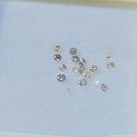 Multiple loose round faceted diamonds placed on a white surface, showcasing different sizes and slight color variations.
