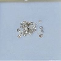 Close-up photo of multiple small loose round cut diamonds clustered on a white background.