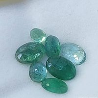 Seven loose emerald gemstones viewed against a light background showing their cabochon cuts and various green hues.