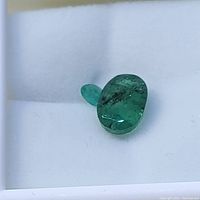 Two emerald gemstones on a white surface, showing size difference and inclusions in the larger stone.