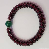 Full view of garnet and green onyx flexible bracelet arranged in circular shape on white background.