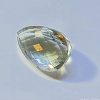 Close-up image of loose 21 carat green amethyst gemstone with pear-shaped faceted cut, translucent light green color with reflective surfaces.