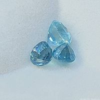 Close-up of three natural blue zircon gemstones on white background showing facets and color.