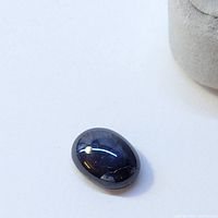 Loose blue sapphire gemstone cabochon on a white surface, oval shape, smooth polished surface with deep blue color.