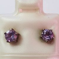 Close-up front view of silver stud earrings with round amethyst stones in prong settings.