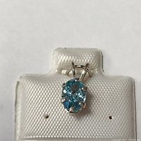 Front view of the silver pendant with oval blue zircon gemstone in a secure four-prong setting on a white display stand.