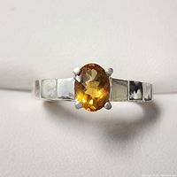 Close-up front view of the silver ring with an oval faceted citrine in a four-prong setting.