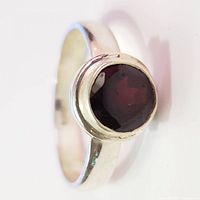 Close-up front view of silver ring with round red garnet stone in bezel setting.