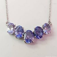 Front close-up showing oval tanzanite stones graduated light to dark blue-purple, set in silver prong settings on chain