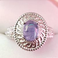 Close-up front view of silver ring with oval cabochon tanzanite center stone surrounded by detailed silver rope and leaf motif design.