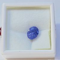 Close-up image of a loose oval cut tanzanite gemstone with a rich blue-purple color displayed in a white cushioned display box.