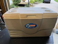 Photo of a large rectangular grey Coleman Xtreme cooler with four molded cup holders on top and textured surface.