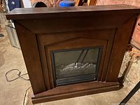 Front view of the large electric fireplace showing wooden mantel and glass firebox with artificial logs inside.