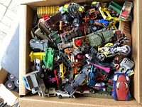 Top-down photo of large box densely packed with various toy vehicles such as cars, motorcycles, and tanks.