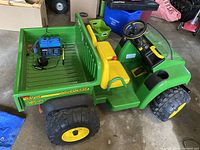 Side view showing green tractor with yellow seats, rear cargo bed containing blue battery and charger
