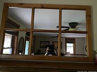 Front view of the rectangular pine framed mirror divided into six smaller mirror panes showing reflection of room interior and person taking photo.
