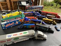 Overview of multiple NASCAR 1/64 toy haulers displayed on a table showing various sponsor themes and paint colors.