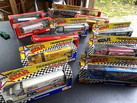 Overview photo of eleven Nascar 1/64 scale toy haulers in original packaging from the Super Star Transporters Series, showing various racing sponsor decals and colors including Hooters Racing and Kodak Film.