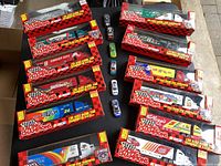 Photo of all 12 NASCAR Racing Champions 1/64 scale toy haulers still in original boxes, arranged on a floor, includes semi trucks and trailers with various team colors and sponsors.