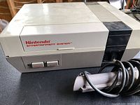 Close-up of the original 1985 Nintendo Entertainment System console showing the power and reset buttons, front cartridge slot, and worn condition with cables attached.