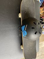 Top view of skateboard with black deck and white wheels, with helmet placed on top showing Pro-Tec blue logo