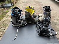 Photo showing three pairs of snowboard boots and two sets of snowboard bindings on top of a snowboard.