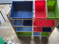 Photo showing front view of storage rack with 12 plastic bins in blue, red, and green.